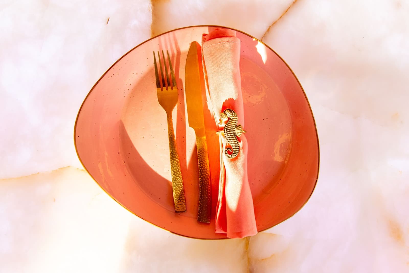 A gold seahorse napkin ring on a blush place setting