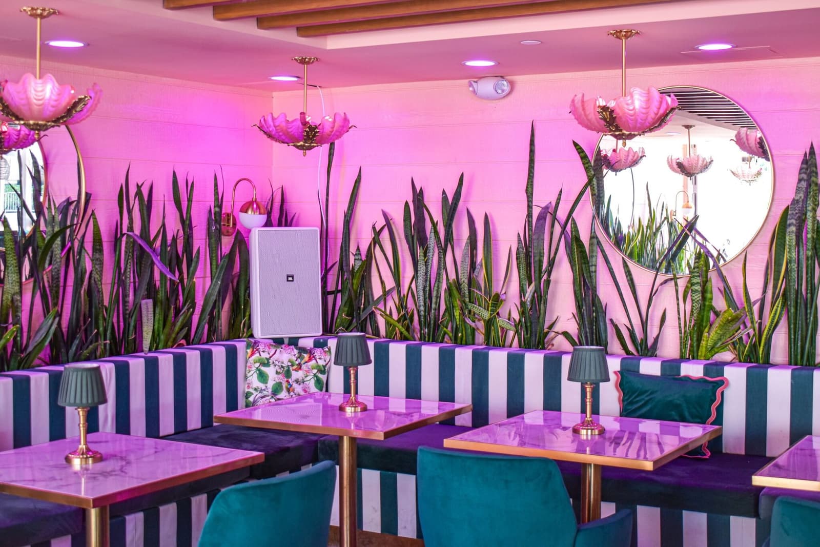 The dining room beneath the floral mural, with striped banquettes and teal velvet chairs