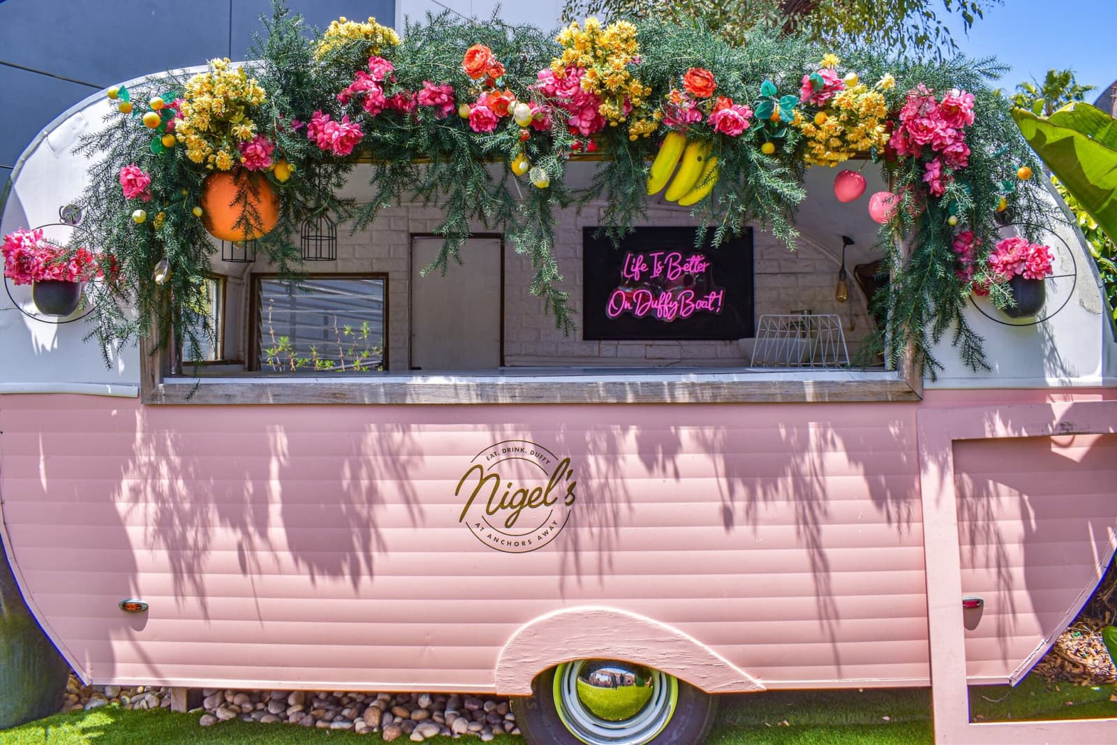 The pink Nigel's caravan bar crowned with blooms and a Duffy-boat neon sign
