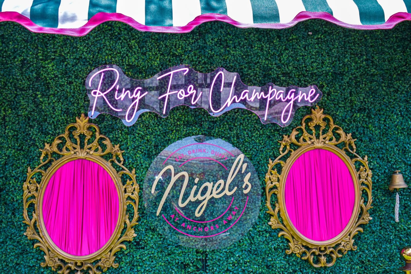 The Ring for Champagne hedge wall with gilded frames, neon, and a brass bell