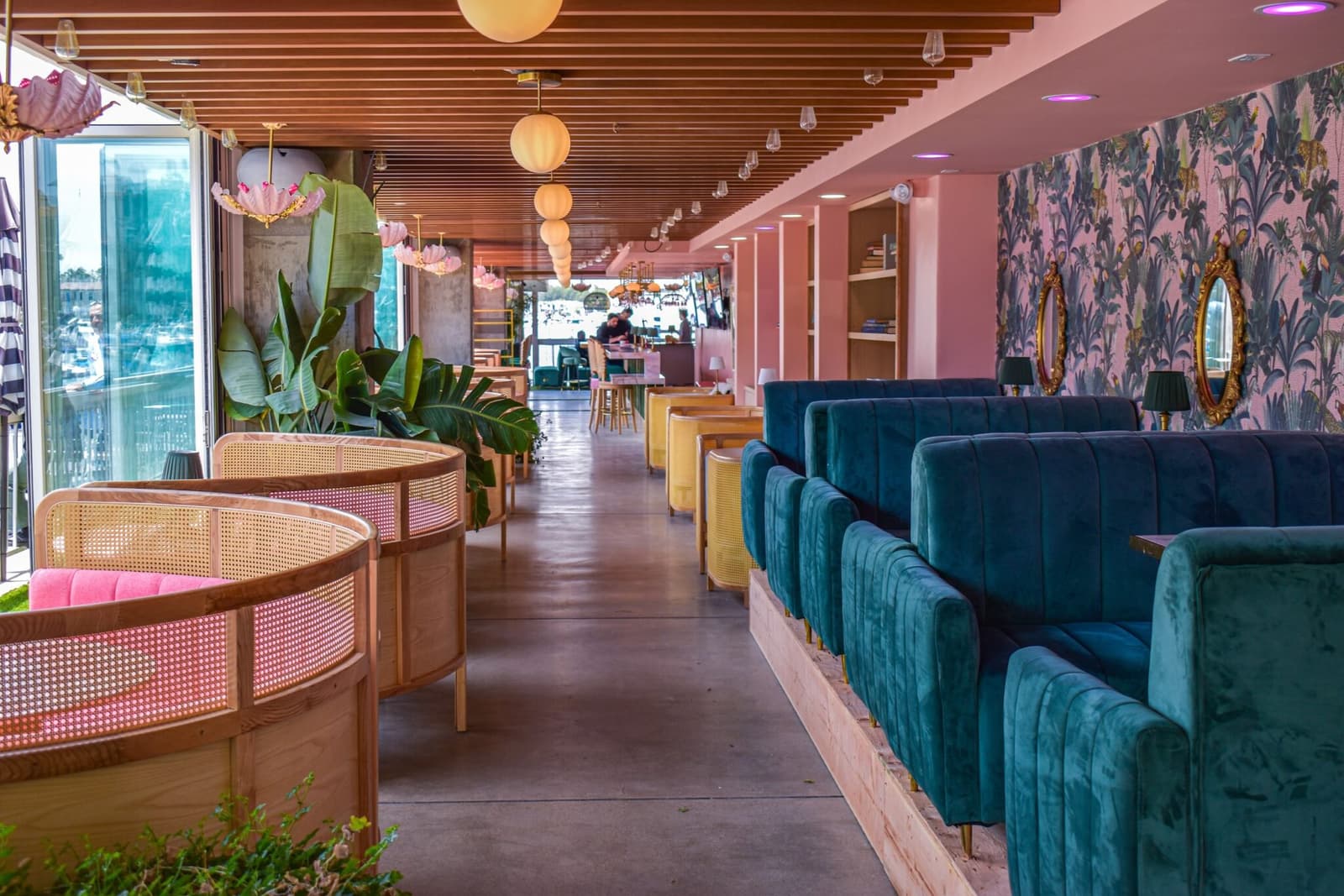 The pink room at golden hour: teal velvet seating, cane chairs, and the marina beyond