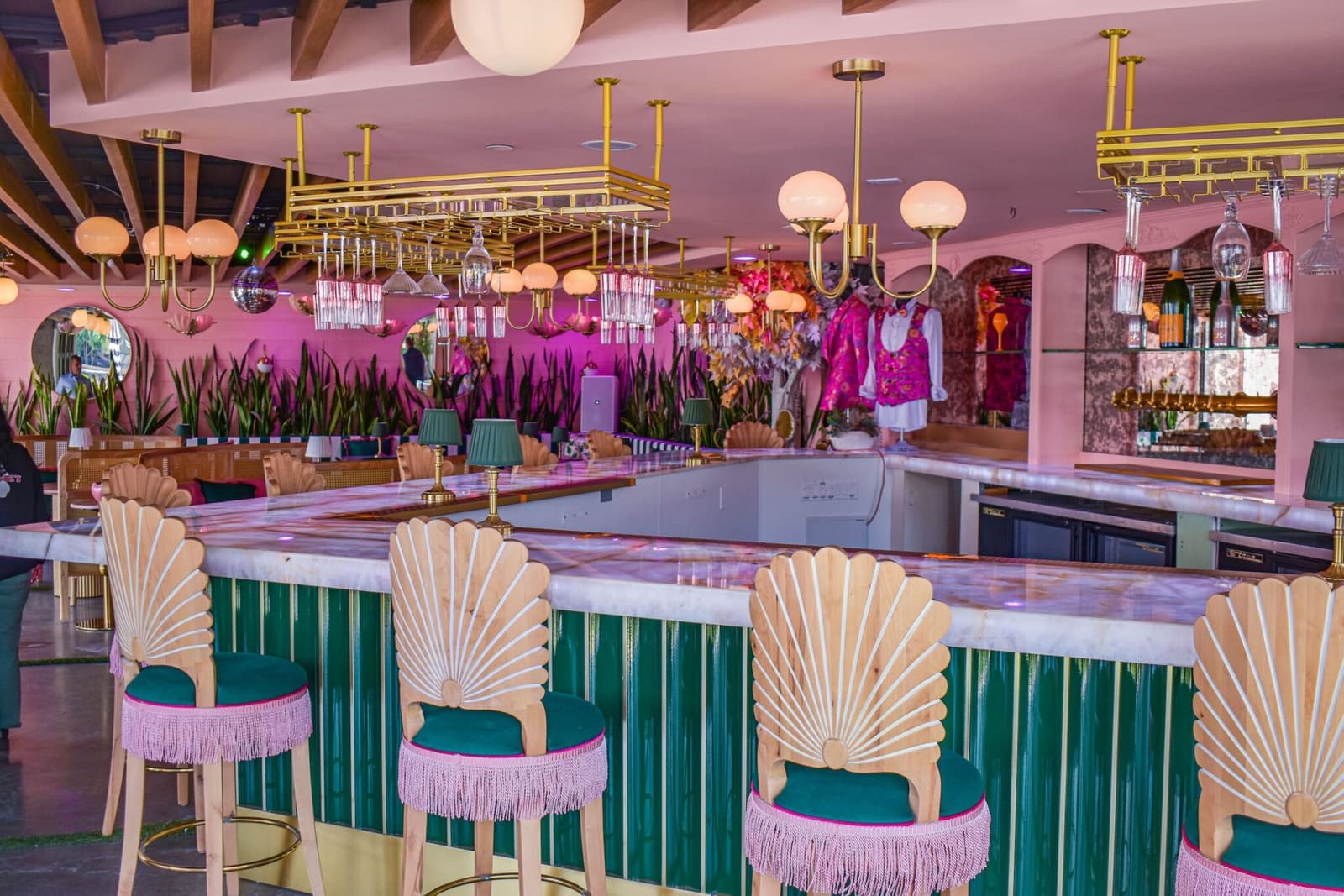 Gold shell-back stools with pink fringe along the marble champagne bar