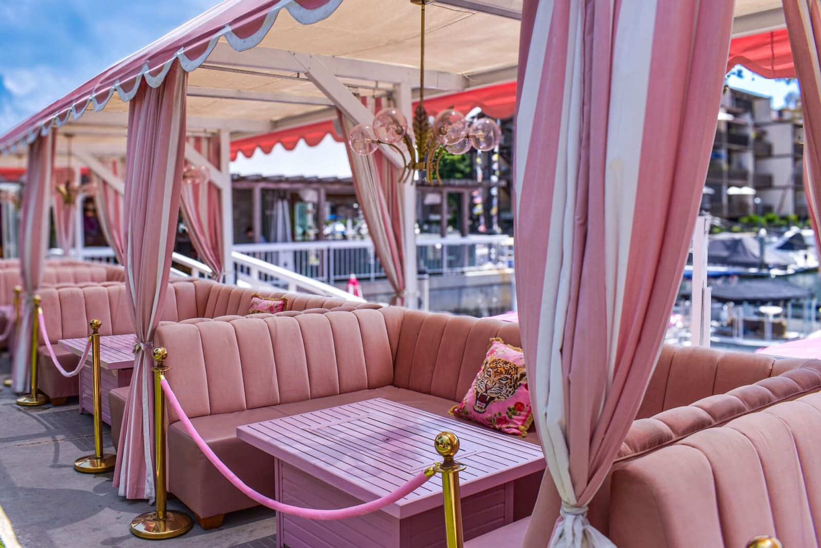 A row of pink waterfront cabana booths draped in stripes over the marina