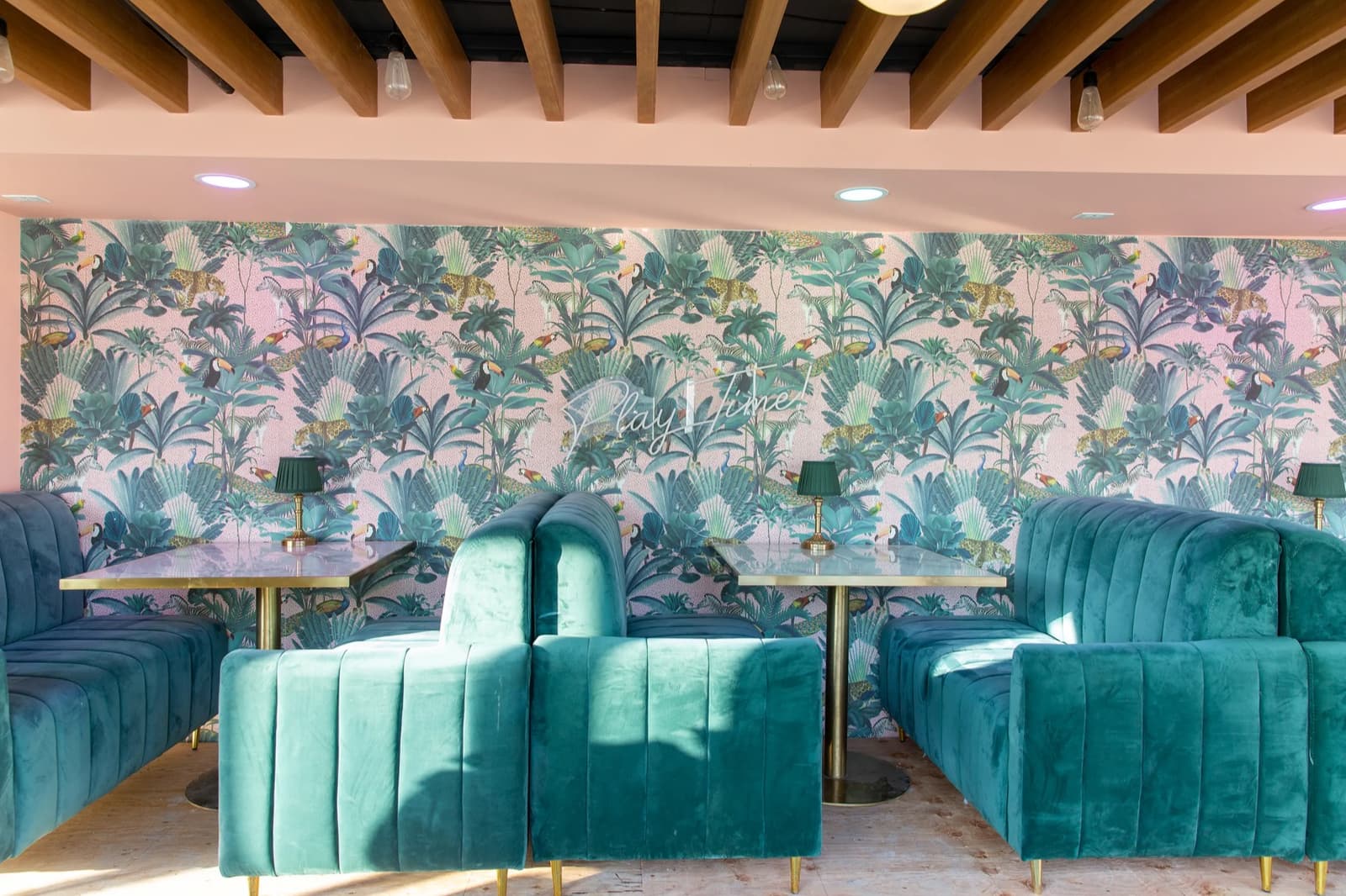 Tropical jungle wallpaper behind deep teal velvet booths and marble tables