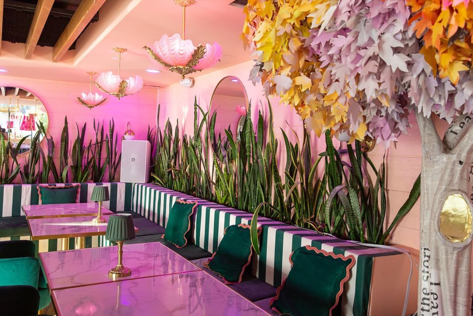 Pink marble tables and velvet banquettes beneath a sculptural paper-leaf tree